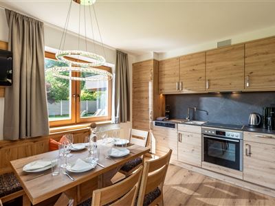 Eine moderne Küche mit Holzmöbeln und einem Esstisch. Das Fenster lässt viel Licht herein und bietet einen Blick ins Freie.