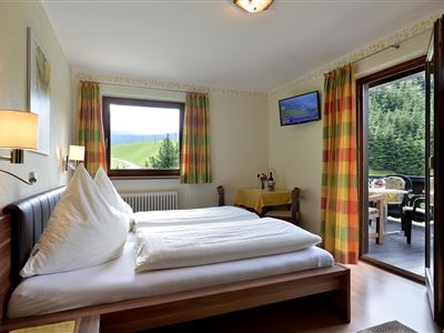 Ein gemütliches Schlafzimmer mit zwei Betten und bunten Vorhängen. Durch die Fenster sieht man einen schönen Ausblick auf die Natur.