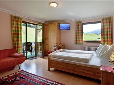 Ein gemütliches Zimmer mit einem Doppelbett und einem roten Sofa. Große Fenster bieten einen schönen Blick auf die Landschaft.