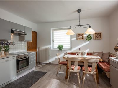 Eine modern eingerichtete Küche mit einem Tisch und Stühlen sowie einem gemütlichen Essbereich. Es gibt helle Wände und eine Fensterfront, die viel Licht hereinlässt.