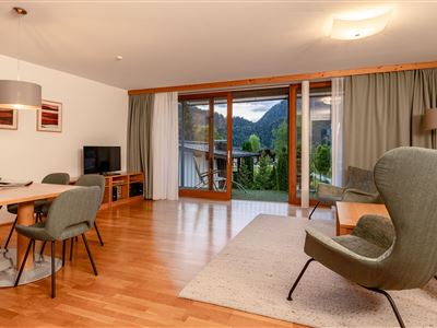 Ein modernes Wohnzimmer mit Holzfußboden und großen Fenstern, die einen Blick auf die Berge bieten. Der Raum ist hell und bietet eine freundliche Atmosphäre mit stilvollen Möbeln.
