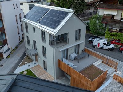 Ein modernes Haus mit Solarpanelen auf dem Dach. Es befindet sich in einer ruhigen Umgebung mit anderen Gebäuden in der Nähe.