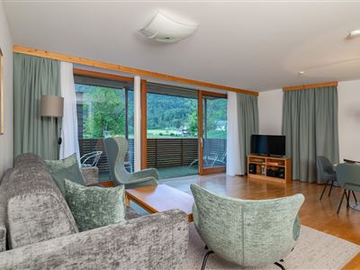 Ein modernes Wohnzimmer mit einem gemütlichen Sofa und stilvollen Stühlen. Große Fenster bieten einen Blick auf die Natur draußen.