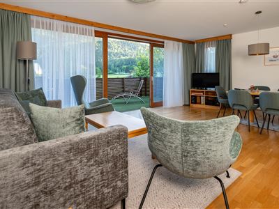 Ein modern eingerichtetes Wohnzimmer mit gemütlichen Möbeln und großen Fenstern. Der Raum bietet Zugang zu einem grünen Außenbereich.