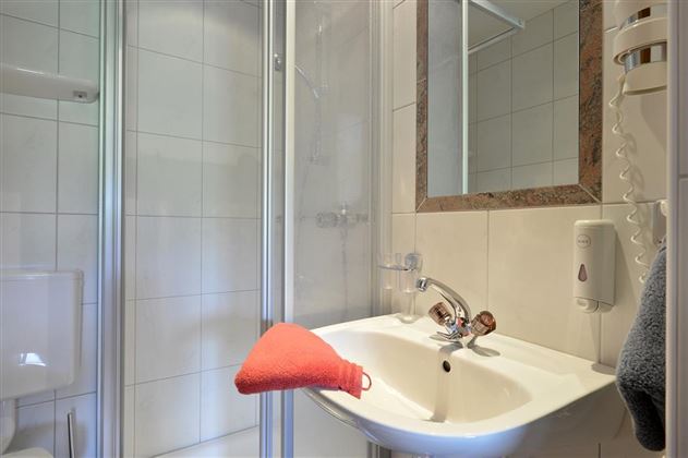 Ein modernes Badezimmer mit einer Dusche und einem Waschbecken. Ein orangefarbenes Handtuch liegt auf dem Waschbecken.