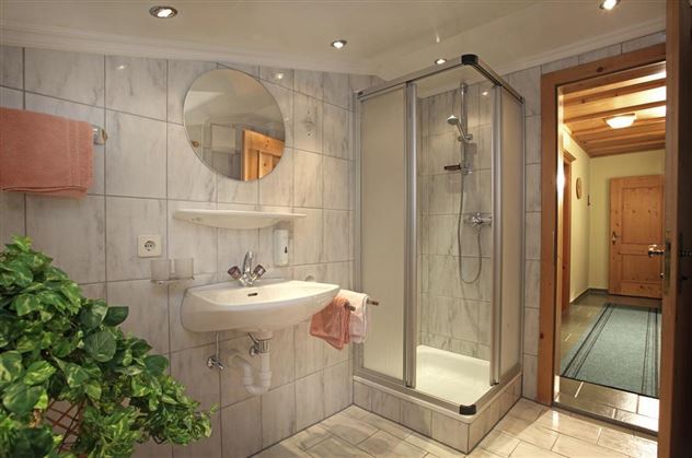 Ein modernes Badezimmer mit einer Dusche und einem Waschbecken. Die Wände sind mit hellen Fliesen verkleidet und es gibt eine schöne Pflanze in der Ecke.