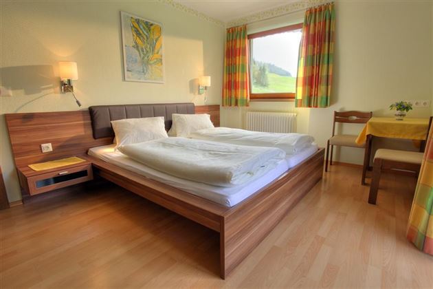 Ein gemütliches Schlafzimmer mit einem Doppelbett und Holzfußboden. Große Fenster bieten einen Blick auf die grüne Landschaft.