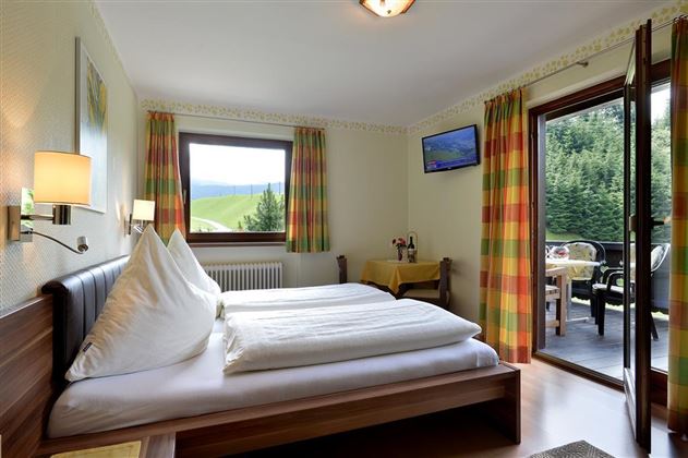 Ein gemütliches Schlafzimmer mit zwei Betten und bunten Vorhängen. Der Raum bietet einen Blick auf die Natur durch ein großes Fenster und eine дверь zur Terrasse.