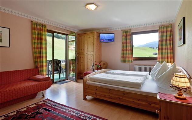 Ein gemütliches Zimmer mit einem Doppelbett, einem roten Sofa und einem Fernseher. Große Fenster bieten einen Blick auf die grüne Landschaft.