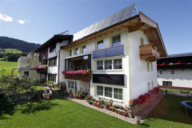Ein modernes Wohnhaus mit mehreren Balkonen und bunten Blumen. Im Hintergrund sind sanfte Hügel und ein klarer Himmel zu sehen.