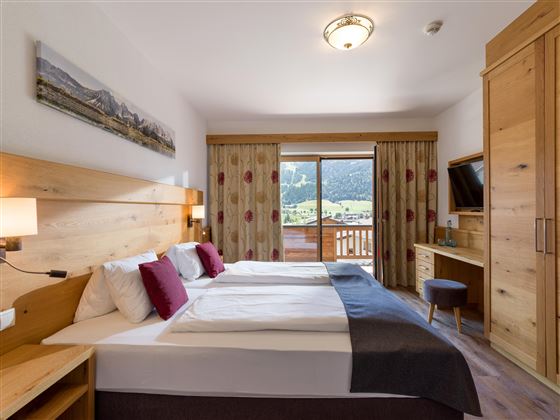 Habitación doble en el Hotel Alpenpanorama en la región de vacaciones Wilder Kaiser con muebles de madera, rincón acogedor y vistas a la naturaleza.