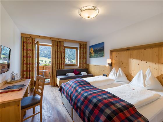 Acogedora habitación doble con muebles de madera, detalles a cuadros y balcón con vistas a la montaña.