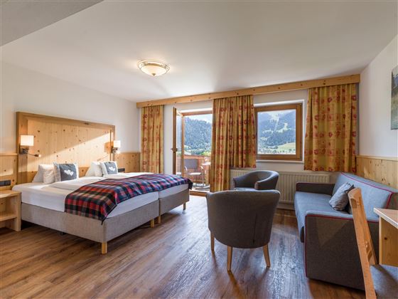 Habitación doble espaciosa en el Hotel Alpenpanorama en la región turística Wilder Kaiser con zona de estar, sofá, escritorio y mucha luz natural.