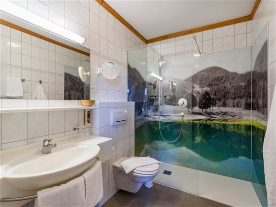 Baño moderno en el Hotel Alpenpanorama en la región turística Wilder Kaiser con ducha, espejo grande y decoración alpina en la pared.