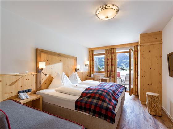 Acogedora habitación doble en el Hotel Alpenpanorama en la región de vacaciones Wilder Kaiser con cama de madera, manta a cuadros y vistas a las montañas.