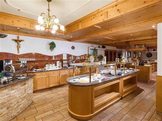 Zona de restaurante luminosa del Hotel Alpenpanorama con buffet, techo de madera y decoración tirolesa.