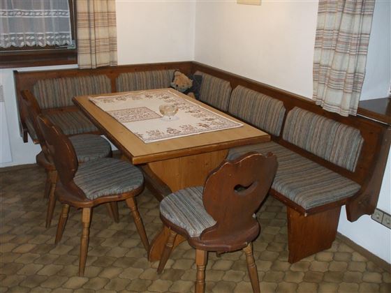 Ein gemütlicher Essbereich mit einer Holzbank und einem Tisch. Die Stühle sind ebenfalls aus Holz und mit gestreiften Bezugstoffen gepolstert.