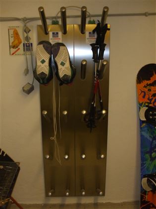 Un secador de botas de esquí. En el gancho cuelgan las botas, al lado hay una tabla de snowboard.