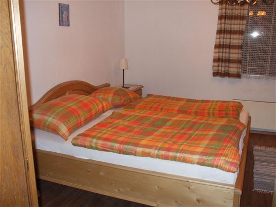 Una acogedora habitación con una cama doble y edredones a cuadros. Las paredes están pintadas de un color claro y hay lámparas de mesita de noche así como cortinas en la ventana.