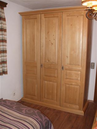 Un armario clásico de madera con tres puertas. El armario está en un dormitorio acogedor.