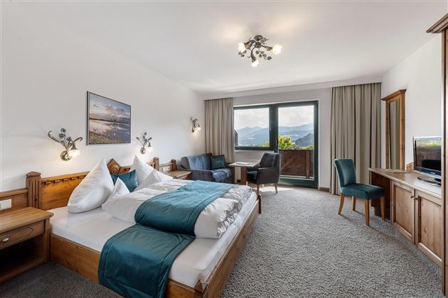 Una habitación de hotel moderna con una cama grande, una mesa y sillas. La vista desde la ventana muestra un hermoso paisaje montañoso.