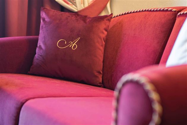 Amor por el detalle: La almohada con el logo en la elegante silla tapizada expresa de manera encantadora la firma de la casa.