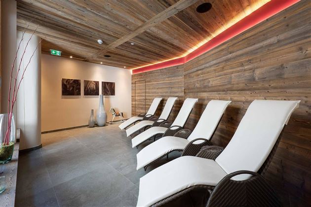 Una zona de spa relajante con modernas tumbonas y paredes revestidas de madera. La luz suave crea una atmósfera tranquila.
