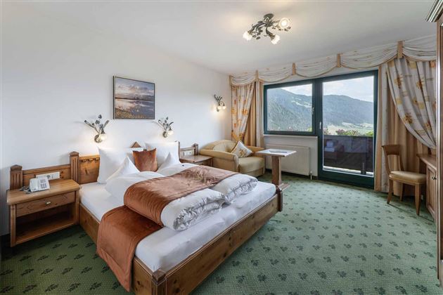 Una habitación de hotel acogedora con dos camas, una mesa y una silla. La ventana ofrece una vista a las montañas.