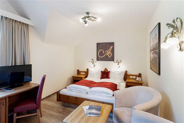 Una acogedora habitación de hotel con una cama doble y ropa de cama roja. Hay un escritorio, un televisor y un sillón cómodo.