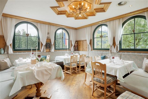 Un restaurante acogedor con manteles y elegantes sillas de madera. Ventanas amplias ofrecen una vista de la naturaleza.