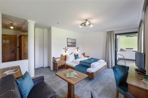Comodidad se encuentra con naturaleza: La amplia habitación doble "Wilder Kaiser" con una decoración elegante, un acogedor rincón de estar y un balcón con vistas a los Alpes tiroleses.