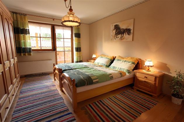 Ein gemütliches Schlafzimmer mit einem Doppelbett und bunten Bettwäsche. Es gibt Holzschränke und einen großen Fenster mit Blick nach draußen.