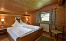 Ein gemütliches Schlafzimmer mit holzvertäfelten Wänden und einem großen Fenster. Es gibt zwei Betten mit weißen Bettdecken, eine Stuhl und warmes Licht von zwei Wandlampen.
