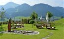 Jardín del Hotel Alpenpanorama en la región turística Wilder Kaiser con tumbonas, banco circular y vistas panorámicas a los Alpes tiroleses.