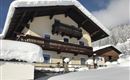 Ein charmantes Chalet im verschneiten Winterlandschaft. Die Fassade ist mit einer dicken Schneeschicht bedeckt und es gibt einen klaren blauen Himmel im Hintergrund.