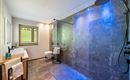 Un baño moderno con una amplia ducha a ras de suelo y azulejos oscuros. La iluminación crea un ambiente agradable.
