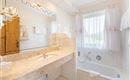 Un baño moderno con una bañera y un gran espejo. Toallas blancas y cortinas claras crean una atmósfera acogedora.