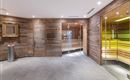 Un área de sauna moderna con revestimiento de madera y luz suave. Las paredes de vidrio ofrecen una vista de la sauna y del acogedor espacio.