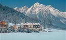Un paisaje invernal pintoresco con montañas cubiertas de nieve en el fondo. En primer plano se encuentra un acogedor hotel, rodeado de árboles nevados.