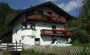 Ein charmantes, zweistöckiges Haus mit Balkonen und bunten Blumen. Es befindet sich in einer grünen Umgebung mit einem klaren Himmel im Hintergrund.