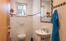 Ein kleines, modernes Badezimmer mit hellem Fliesenboden. Es sind Blumen und ein Handtuch sichtbar, sowie ein Fenster, das Tageslicht hereinlässt.