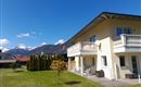 Ein modernes Haus mit einem großen Garten und Blick auf die Berge. Der Himmel ist klar und blau.