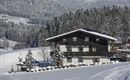 Ein charmantes chalet im Schnee, umgeben von schneebedeckten Bäumen und Bergen. Die Landschaft ist malerisch und friedlich.