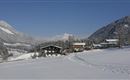 Eine malerische Winterlandschaft mit schneebedeckten Hügeln und Häusern. Der Himmel ist klar und die Umgebung strahlt Ruhe und Frieden aus.