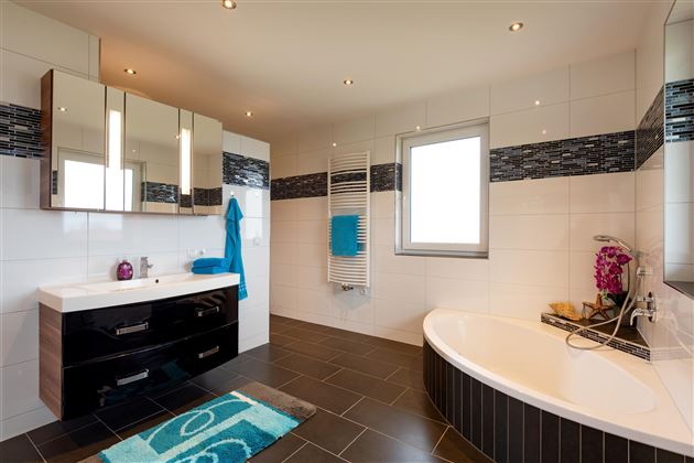 Ein modernes Badezimmer mit einer freistehenden Badewanne und einem stilvollen Waschbecken. Die Wände sind hell gefliest, und es gibt eleganten Raum mit attraktiven Akzenten.