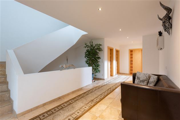 Ein moderner Flur mit heller Beleuchtung und einer eleganten Treppe. Links steht ein Sofa und eine Pflanze sorgt für eine angenehme Atmosphäre.