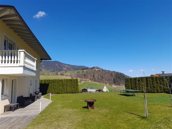 Ein großes, gepflegtes Grundstück mit einer grünen Wiese und einem Ausblick auf die Berge. Das Wetter ist klar und sonnig, ideal für entspannte Stunden im Freien oder zum Grillen.