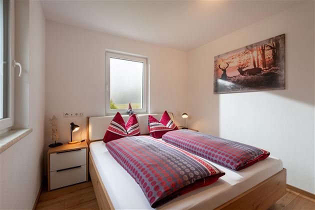 Ein gemütliches Schlafzimmer mit zwei Betten und roten Kissen. An der Wand hängt ein Bild einer Waldlandschaft.
