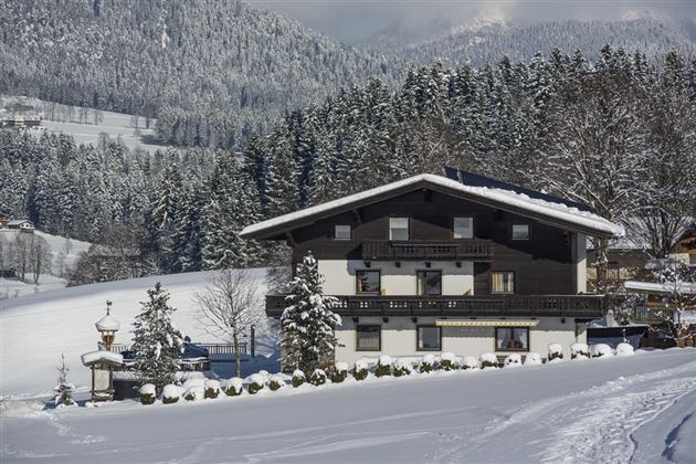 Ein charmantes chalet im Schnee, umgeben von schneebedeckten Bäumen und Bergen. Die Landschaft ist malerisch und friedlich.