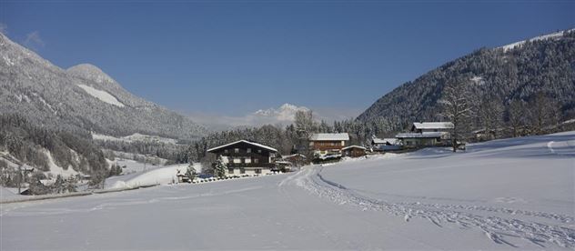 Eine malerische Winterlandschaft mit schneebedeckten Hügeln und Häusern. Der Himmel ist klar und die Umgebung strahlt Ruhe und Frieden aus.